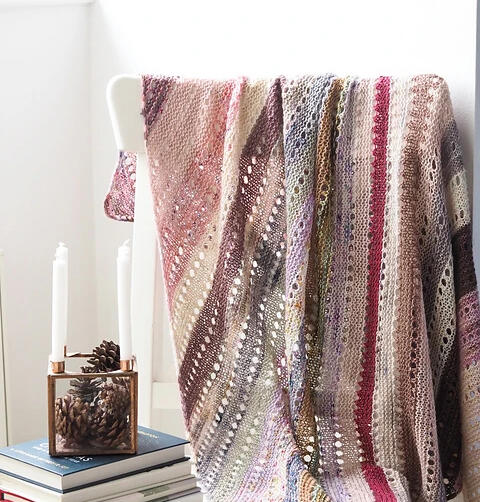 A rectangular knitted throw blanket with stripes of colour and eyelets